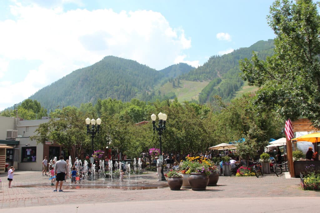 brick pedestrian walk way with water fountains and green mountains in background